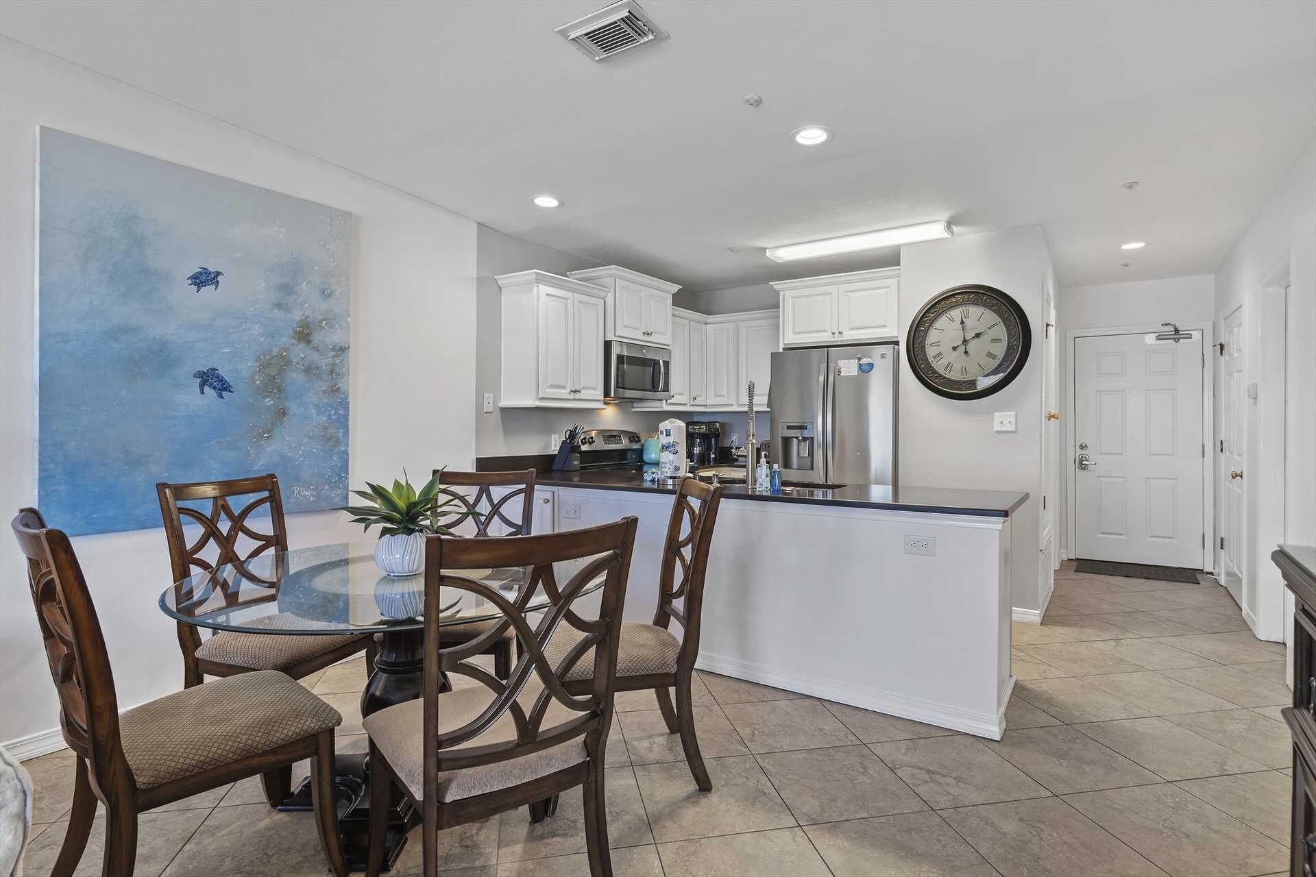 A modern kitchen with white cabinets, a central island, and a dining area with a glass table and wooden chairs.
