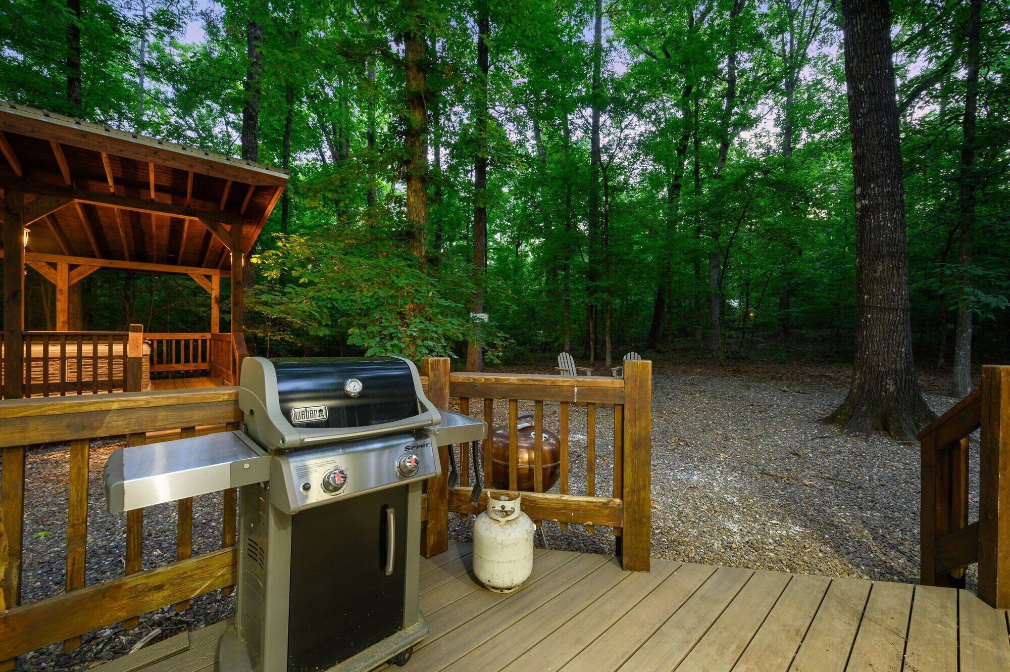 Un barbecue portatif avec une bouteille de gaz et une terrasse en bois dotée d’une rambarde, le tout entouré d’arbres.