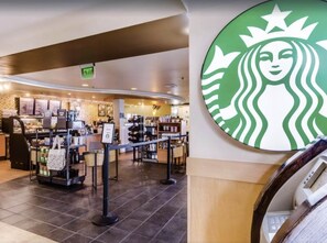 Interno di un bar Starbucks, con un bancone, vetrine espositive e un cartello che indica un'uscita.