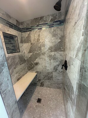 A shower with a marble wall, a bench, and a drain.