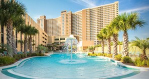 Un hotel con una amplia piscina, palmeras y una fuente.