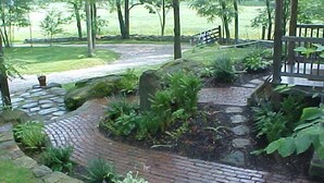A brick pathway leading through a landscaped garden with stone borders and various plants.