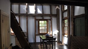 A rustic room with exposed wooden beams, a wooden table with chairs, and a window with a view of greenery.