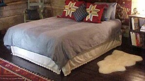 A bedroom with a large bed, a patterned tapestry, and a wooden floor.