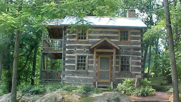 A log cabin with a front door, a balcony, and a stone pathway leading to the entrance.