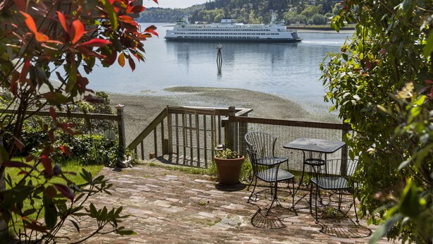 A patio with a table and chairs overlooking a lake with a cruise ship in the distance. - Stunning Beach Suite, great mountain & water views, near downtown Winslow, Cozy. (Bainbridge Island)
