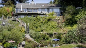 A large house with a balcony, surrounded by lush greenery and a stone wall. - Stunning Beach Suite, great mountain & water views, near downtown Winslow, Cozy. (Bainbridge Island)