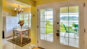 A dining area with a table and chairs, a chandelier, and a view of a green landscape through a glass door. - Stunning Beach Suite, great mountain & water views, near downtown Winslow, Cozy. (Bainbridge Island)