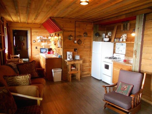 L’intérieur chaleureux d’un chalet avec un plancher en bois, un coin repas comprenant une table et des chaises, une cuisine équipée d’un réfrigérateur et d’une cuisinière, et un salon avec un canapé et un fauteuil.
