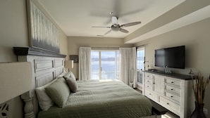 A bedroom with a bed, a ceiling fan, a TV, and a view of the ocean.