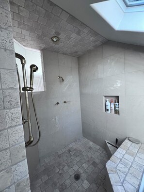 A shower with a glass door, a tiled floor, and a small shelf with toiletries.