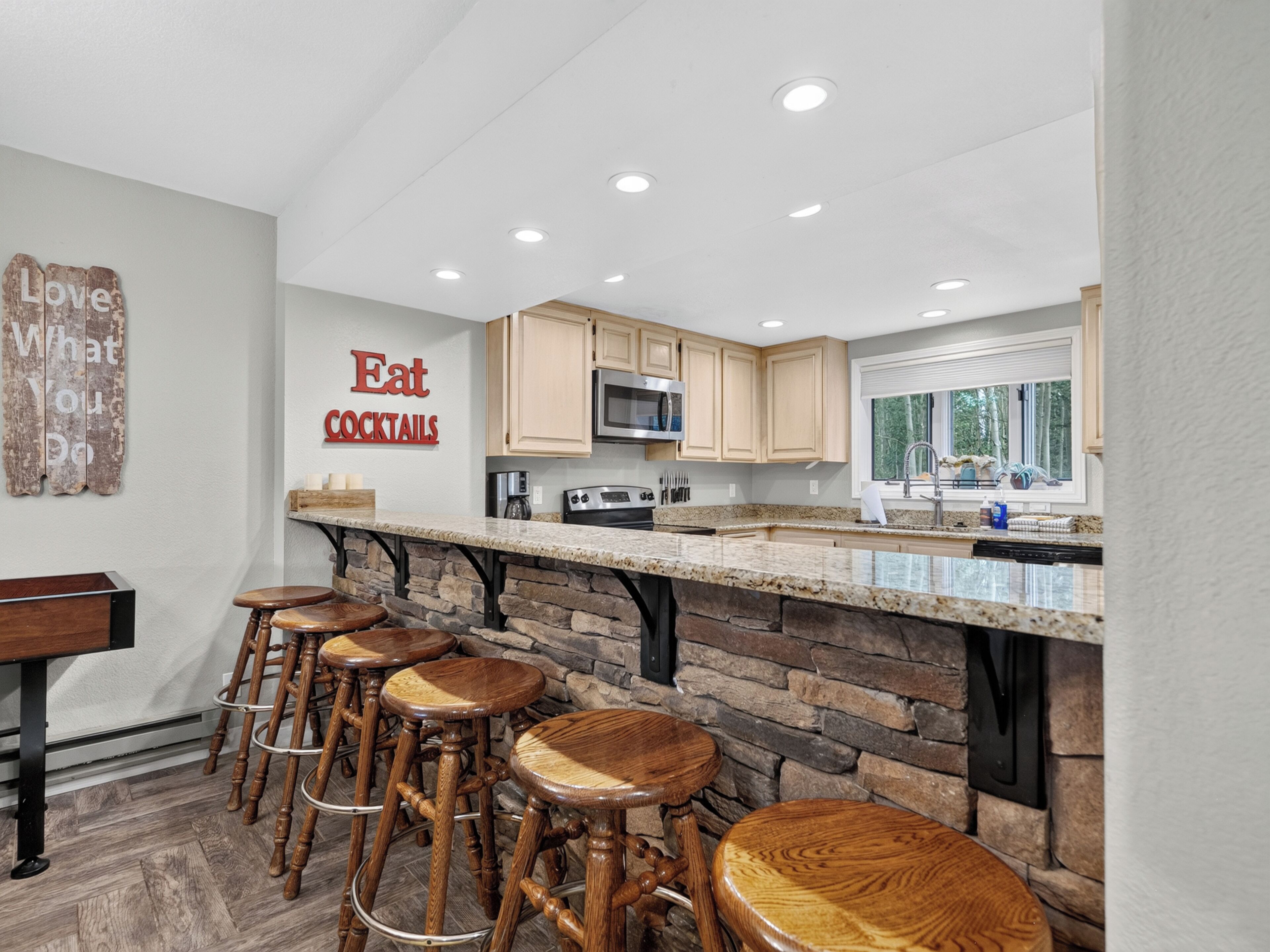 A kitchen with a stone accent wall, wooden bar stools, and a sign that says 'Eat Cocktails.'
