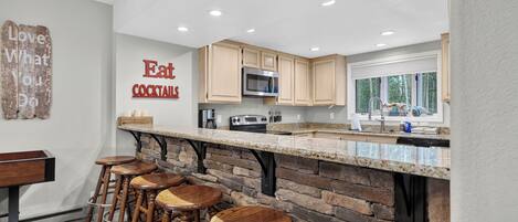 A kitchen with a stone accent wall, wooden bar stools, and a sign that says 'Eat Cocktails.'