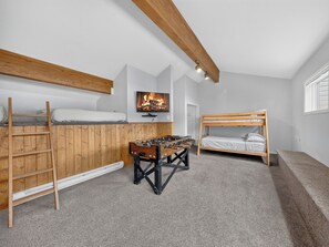 A room with bunk beds, a foosball table, and a television mounted on the wall.