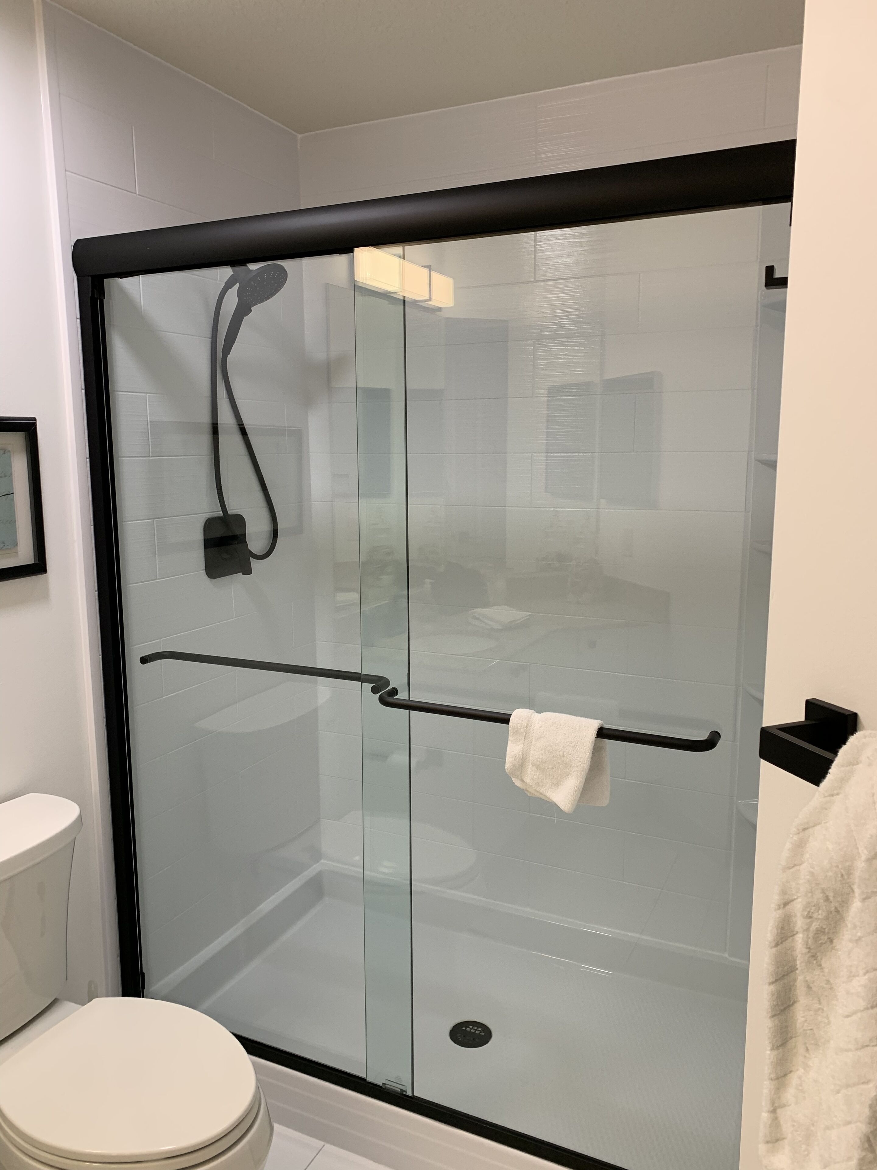 A modern bathroom with a glass-enclosed shower, a black towel rack, and a toilet.