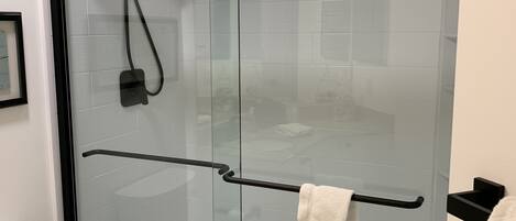 A modern bathroom with a glass-enclosed shower, a black towel rack, and a toilet.