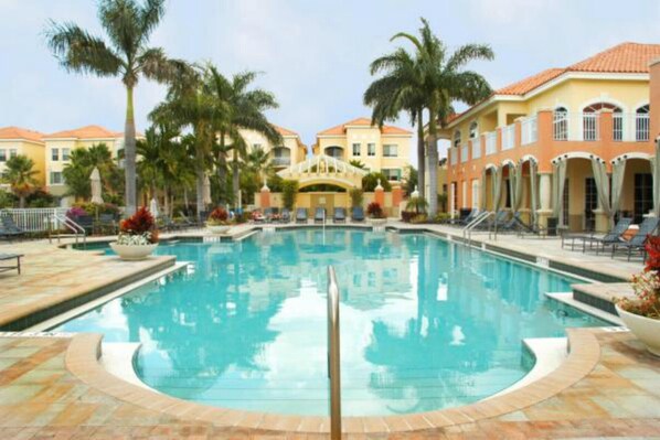 A swimming pool surrounded by palm trees and a building with a tiled roof. - FABULOUS Turn-Key Condo in an Exclusive Gated Community - Palm Beach Gardens (Palm Beach Gardens)