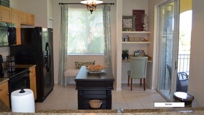 A kitchen with a black refrigerator, a sink, a dining table with a bowl, and a window with curtains. - FABULOUS Turn-Key Condo in an Exclusive Gated Community - Palm Beach Gardens (Palm Beach Gardens)