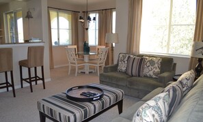 Un salon comprenant un canapé, un pouf et un coin repas avec des chaises et une table.