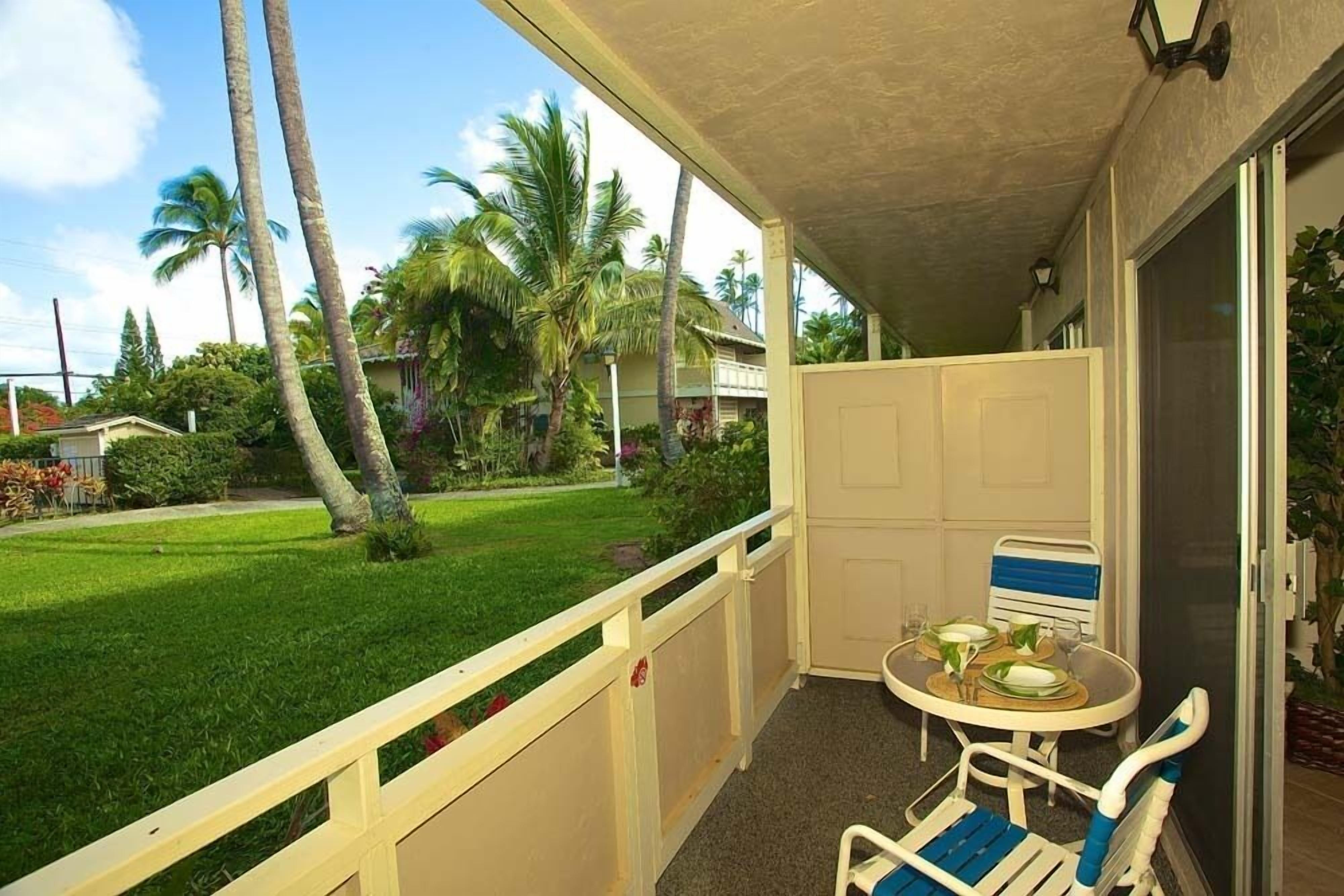 A balcony with a table and chairs, overlooking a lawn with palm trees.