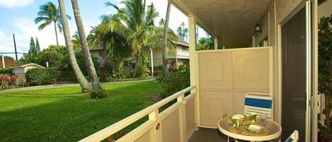 A balcony with a table and chairs, overlooking a lawn with palm trees.