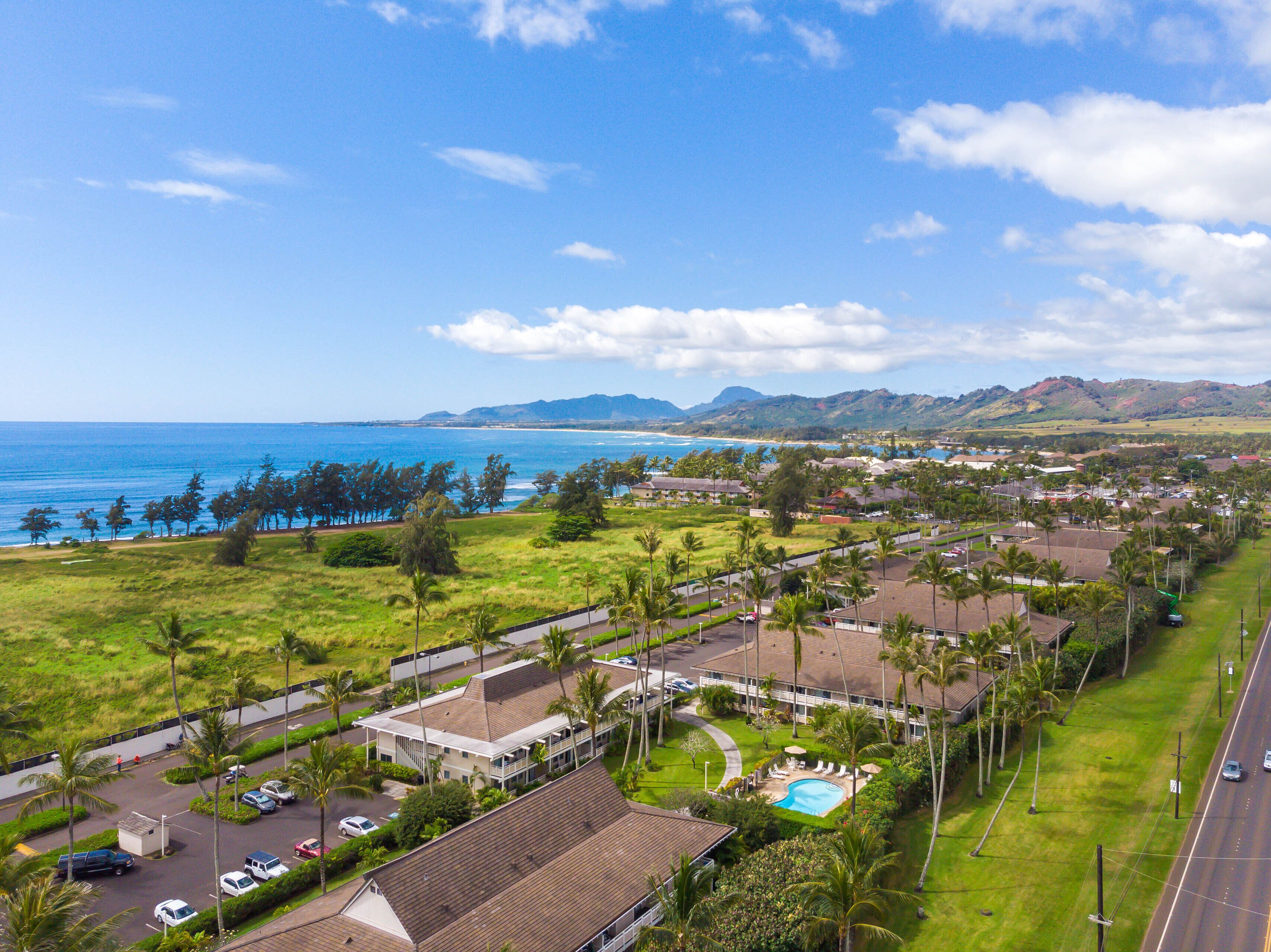 A coastal residential area with a swimming pool, houses, and a road.