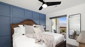 Ein Schlafzimmer mit Bett, Deckenventilator, Fenster und Blick ins Freie.