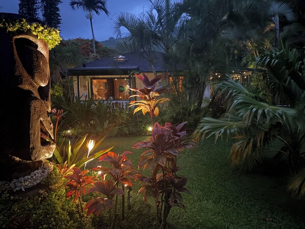 Een tropische tuin met een huis, palmbomen en een stenen gebouw.