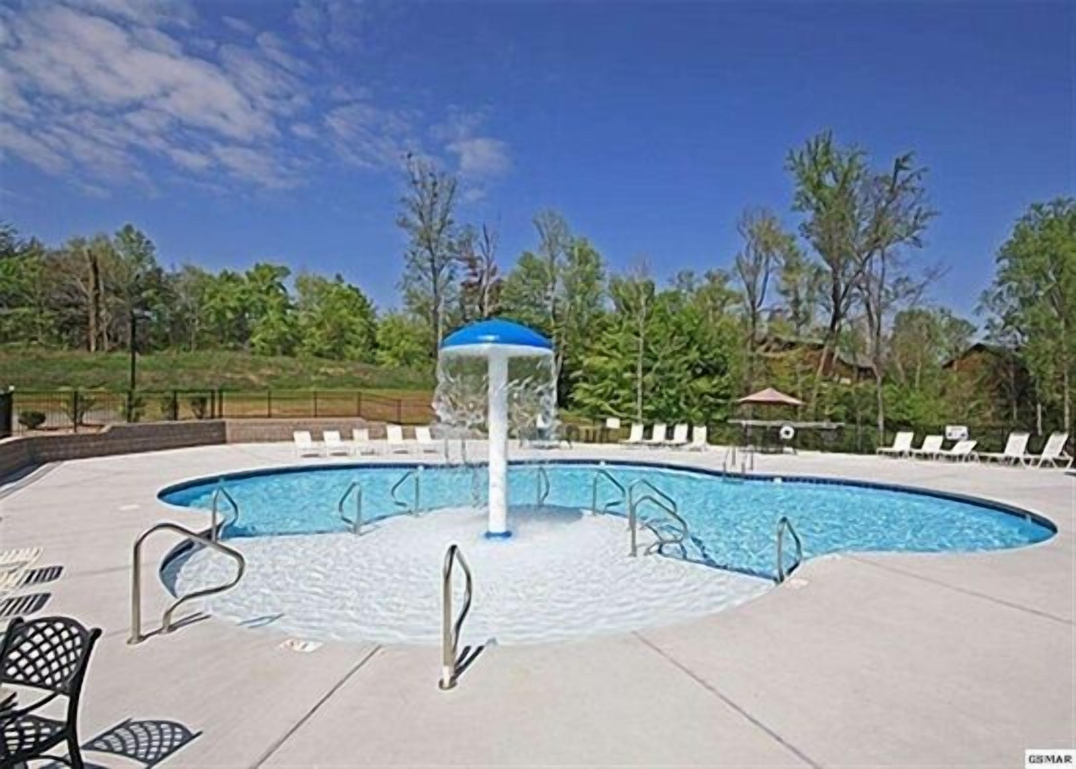 A swimming pool with a water fountain, surrounded by lounge chairs and a gazebo.