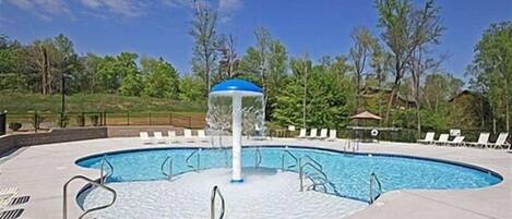 A swimming pool with a water fountain, surrounded by lounge chairs and a gazebo.