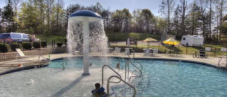 A swimming pool with a water fountain, surrounded by lounge chairs and a camping area.