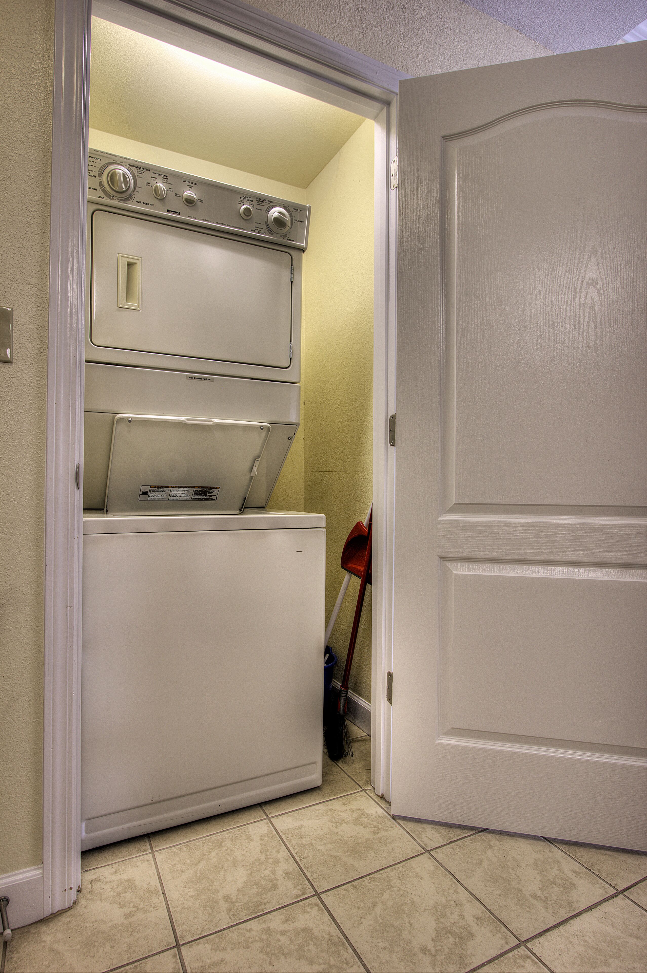 A laundry room with stacked washers and dryers, a broom, and a door.