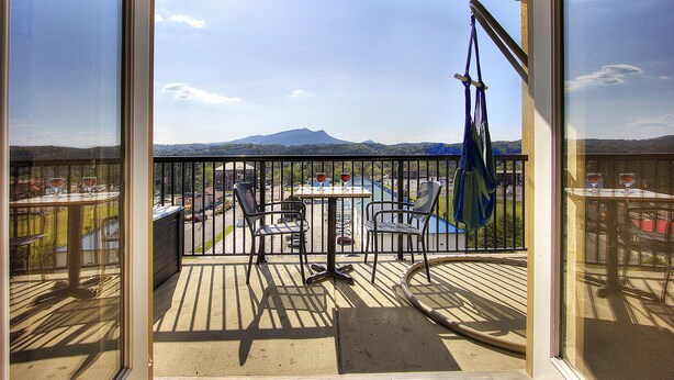 Ein Balkon mit Tisch und Stühlen, Blick auf einen Berg und ein Pool im Hintergrund.