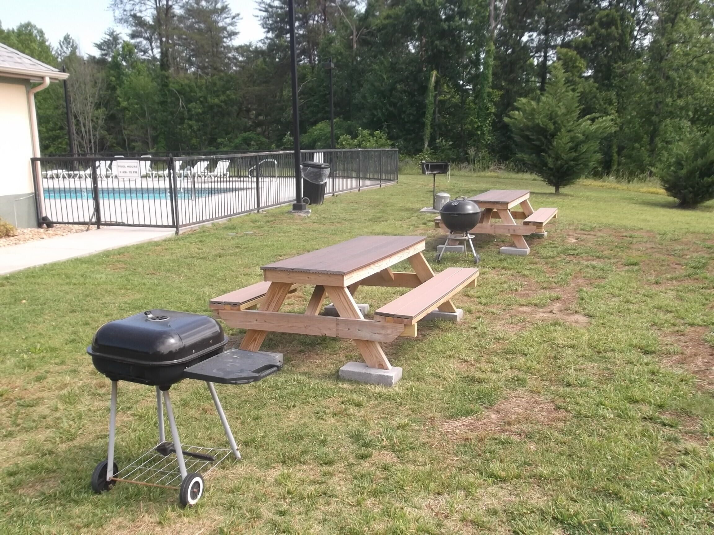 Patio trasero con mesas de picnic, una parrilla y una piscina.