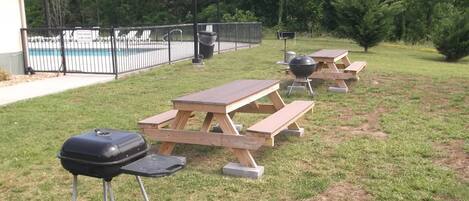 A backyard with picnic tables, a barbecue grill, and a pool.