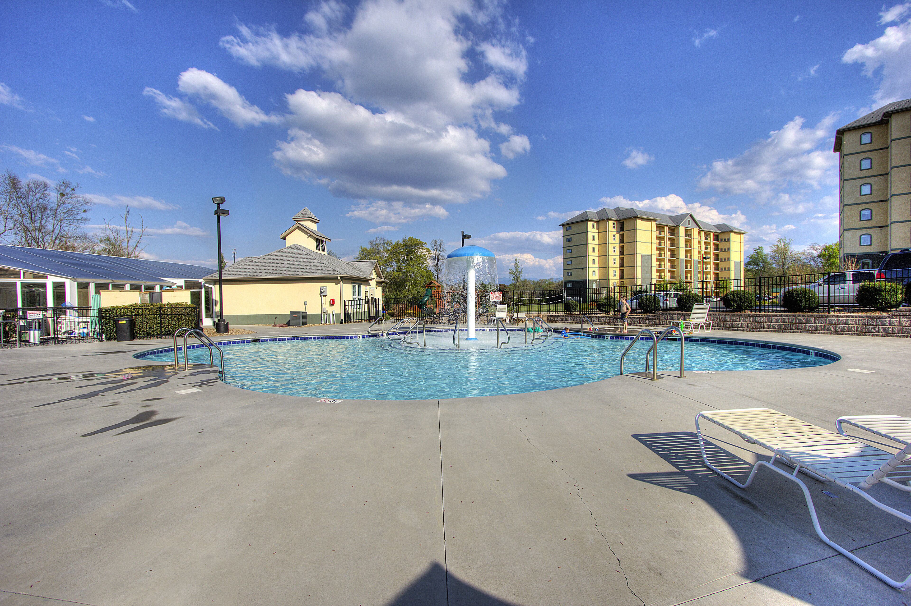 A swimming pool with a fountain, surrounded by lounge chairs and a fence.