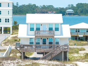 A beachfront building with a balcony, a staircase leading to the entrance, and a view of the water.