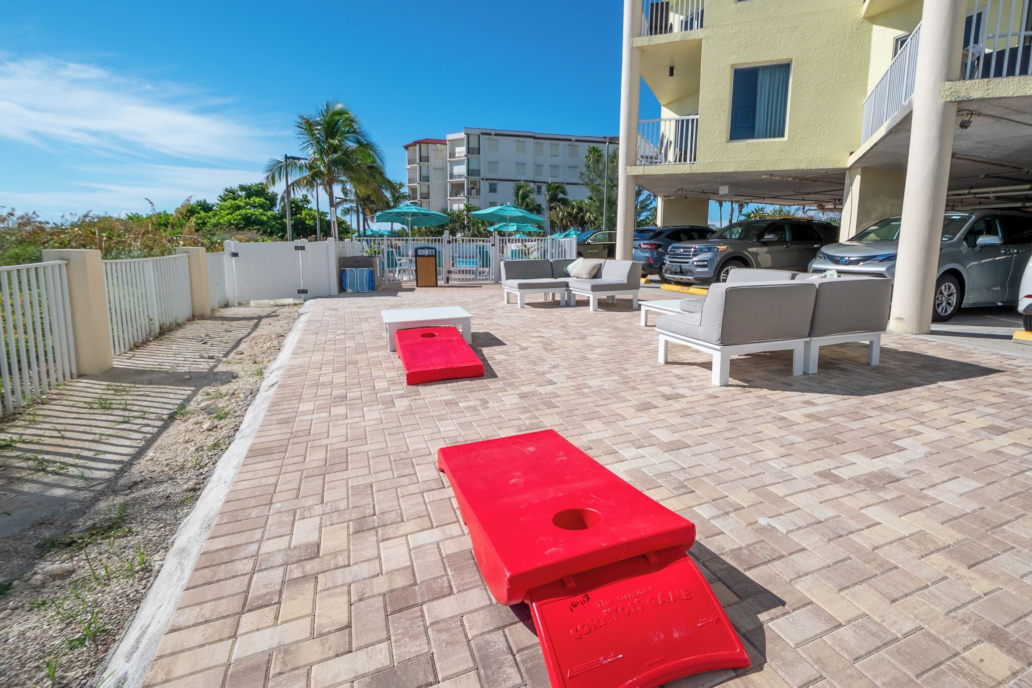 An outdoor seating area with red benches, a poolside area with umbrellas, and a building with balconies in the background.
