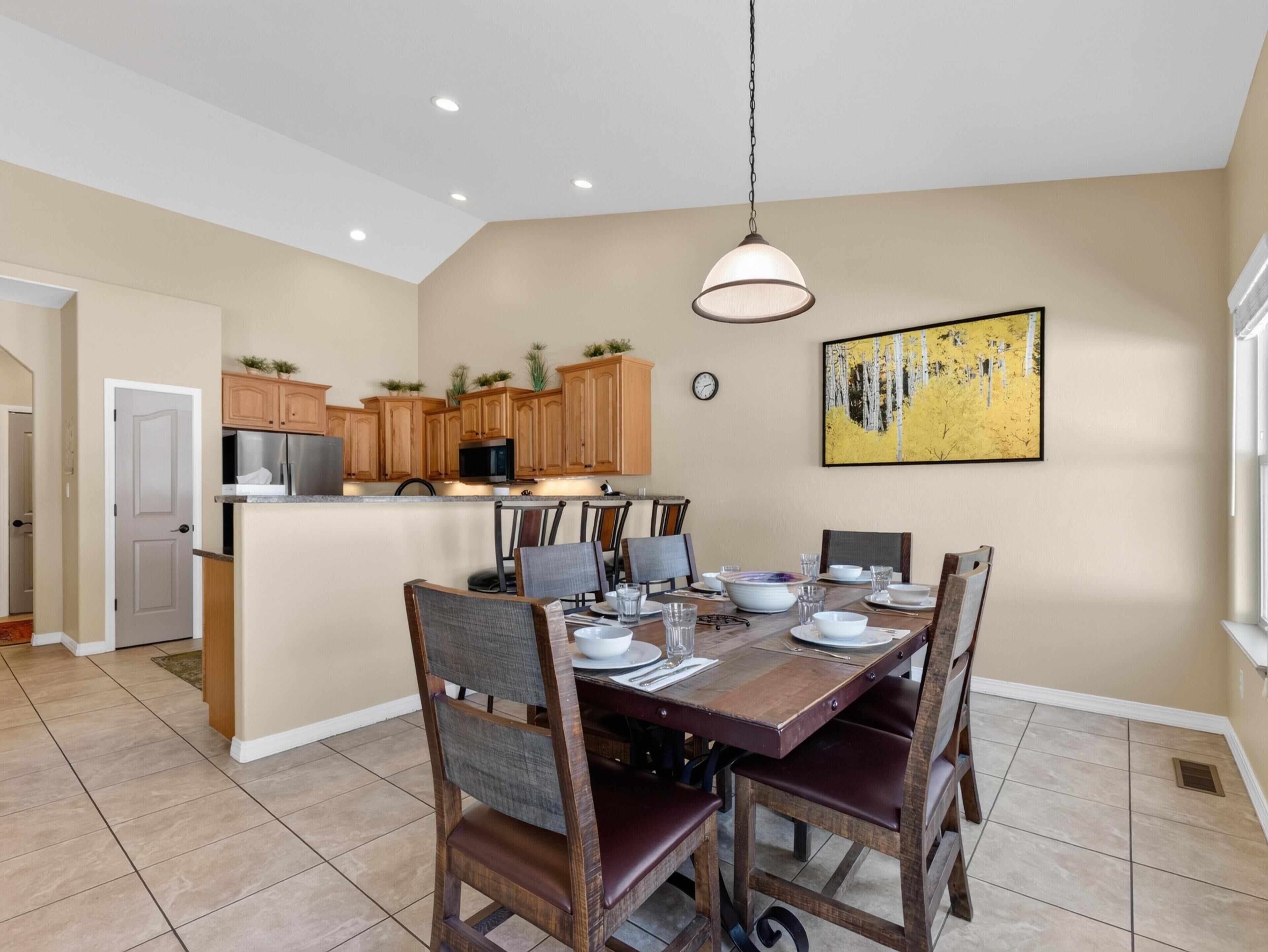 Un coin repas avec une table et des chaises en bois, une cuisine à l’arrière-plan et un tableau accroché au mur.