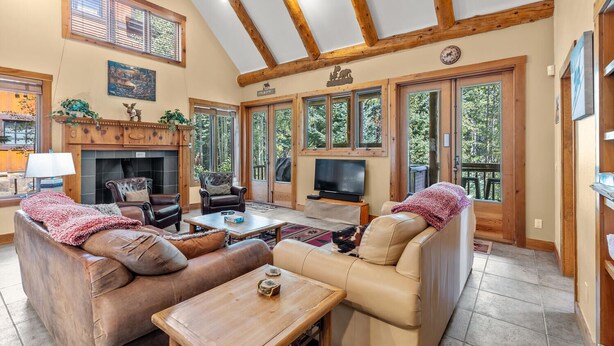 Una sala de estar acogedora con sofás de cuero, chimenea, televisor y ventanas amplias que ofrecen vistas al exterior.
