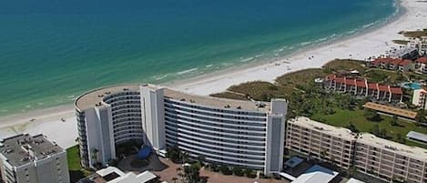 A beachfront hotel with a curved building, multiple balconies, and a beach view.