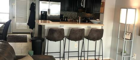 A modern kitchen with dark cabinetry, a stainless steel refrigerator, and a bar area with stools.