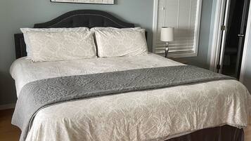 A neatly made bed with a patterned bedspread and pillows, a bedside lamp, and a framed artwork on the wall.
