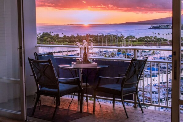 A balcony with a table and chairs overlooking a marina with boats and a sunset view.