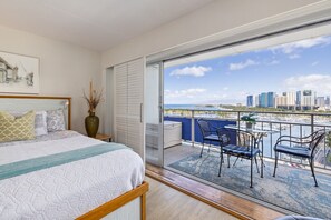 Ein Schlafzimmer mit einem großen Bett, einer Glasschiebetür, die auf einen Balkon mit Blick auf einen Yachthafen und eine Stadtsilhouette führt.
