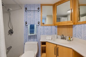 A bathroom with a shower, toilet, wooden cabinets, a sink, and a mirror.