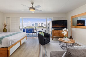 A hotel room with a balcony, a bed, a TV, a sofa, and a small table with flowers.