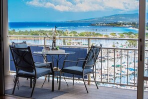 A balcony with a table and chairs, overlooking a marina and the ocean.
