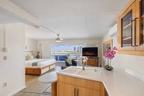 Ein modernes Schlafzimmer mit Bett, einer kleinen Sitzecke, einer Küchenzeile und einem großen Fenster mit Blick auf die Stadt.