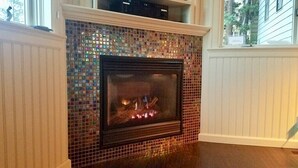Une cheminée ornée d’un décor en mosaïque, avec une étagère au-dessus et une vue sur l’extérieur par une fenêtre.